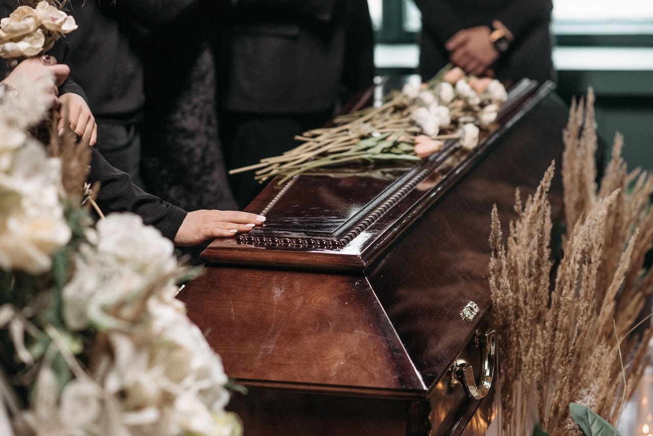 a hand and flowers placed on casket at funeral