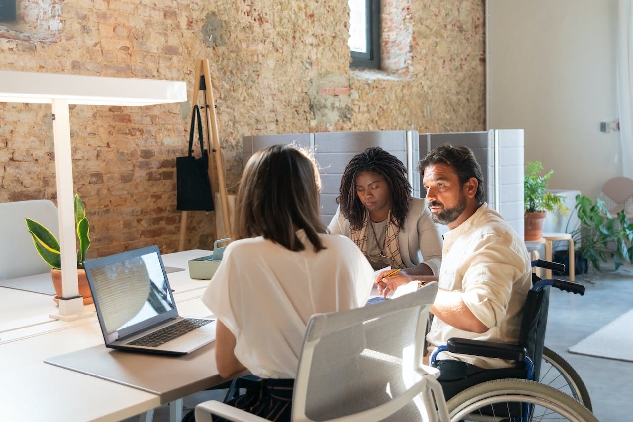 man in a wheelchair talking to two women at desk