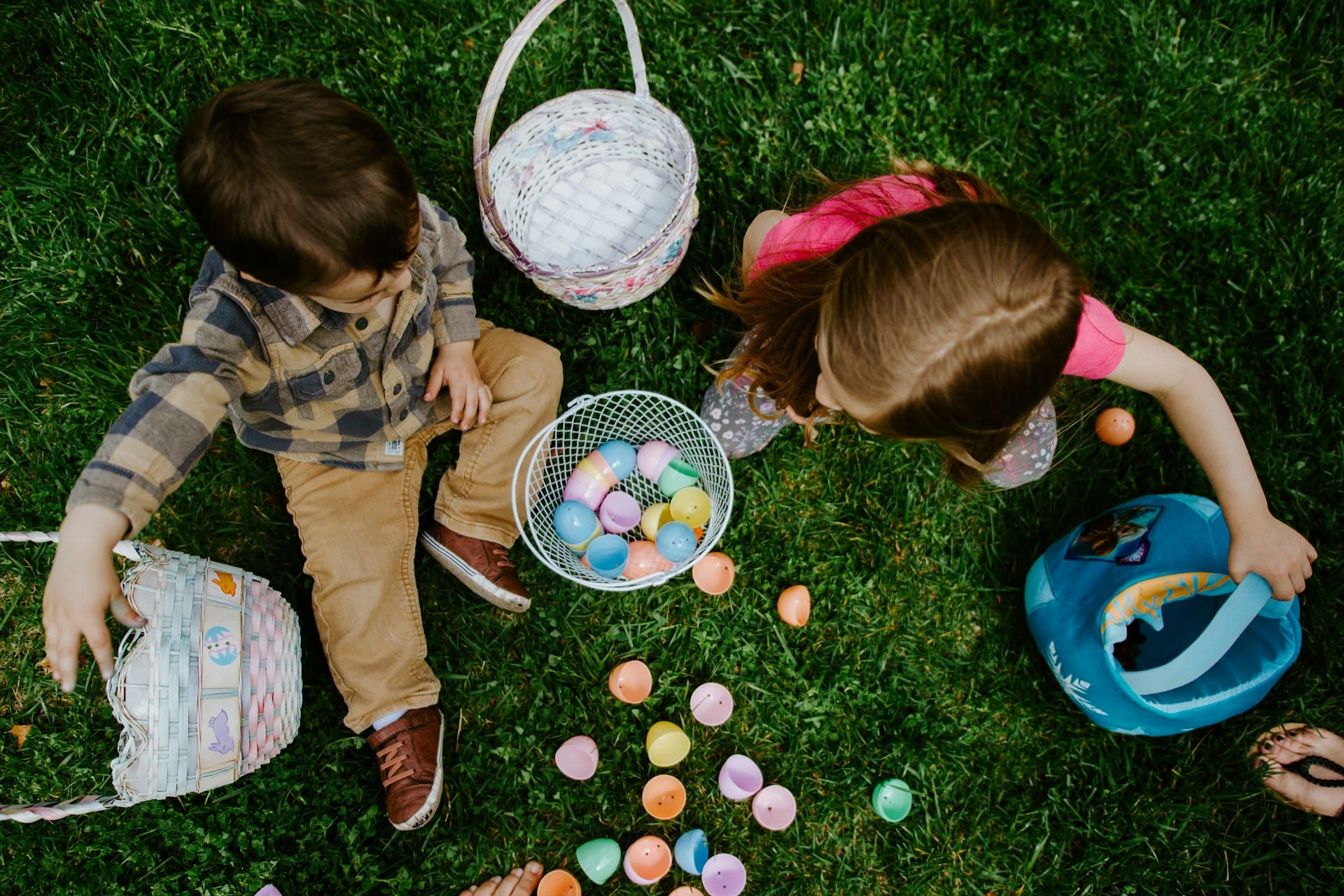 two children sitting in grass counting collected easter eggs
