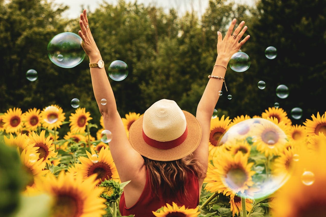 woman standing in field of sunflowers and bubbles with hands raised