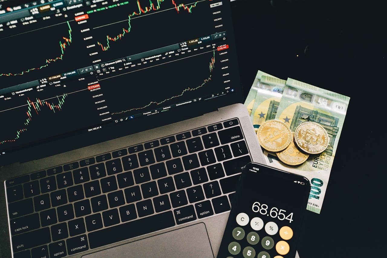 Bitcoin and paper money on table with cellphone and laptop open to graphs