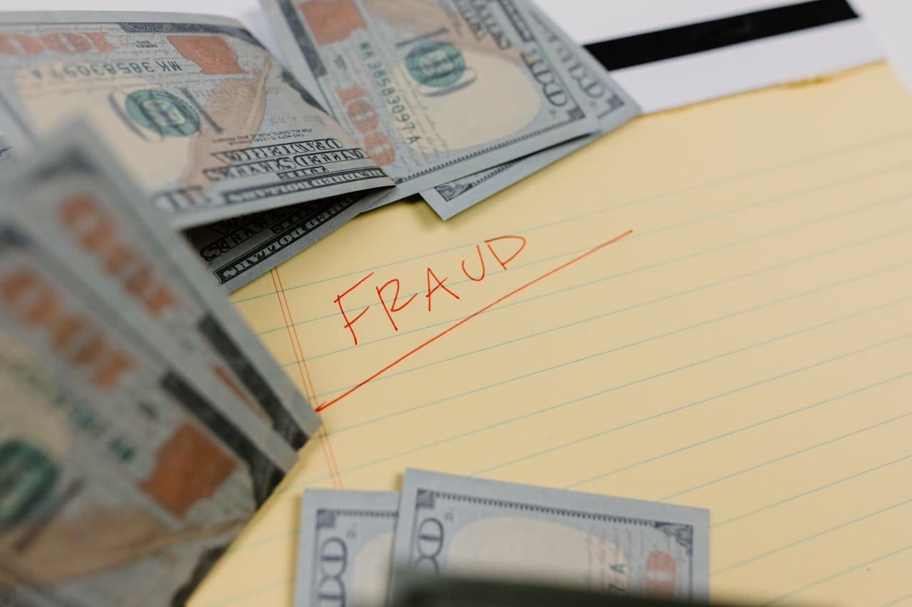 The word 'Fraud' written in red on a yellow paper surrounded by money.