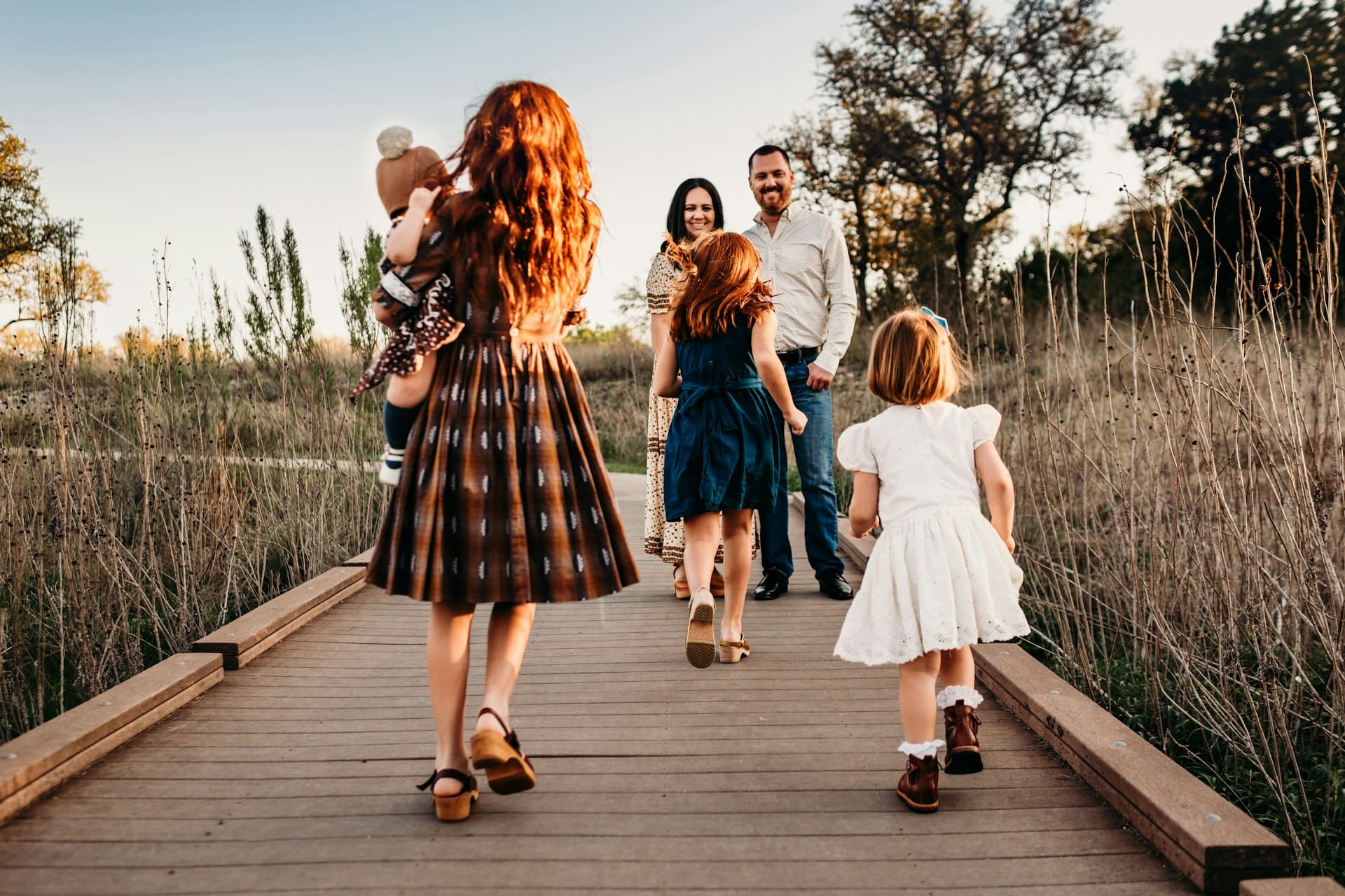 A mother and father standing on a bridge while their four young children run to them.